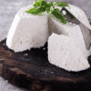 Soft white cheese on board with basil leaves and knife on gray surface.