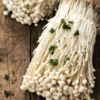 Close-up of enoki mushrooms on wood, garnished with green herbs.