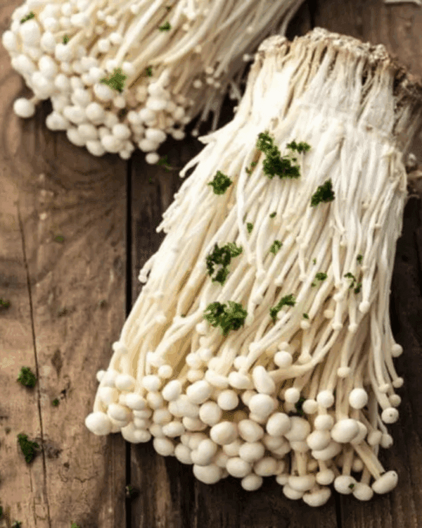 Close-up of enoki mushrooms on wood, garnished with green herbs.
