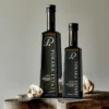 Two Pukara Estate garlic-flavored olive oil bottles on wood, surrounded by garlic cloves.