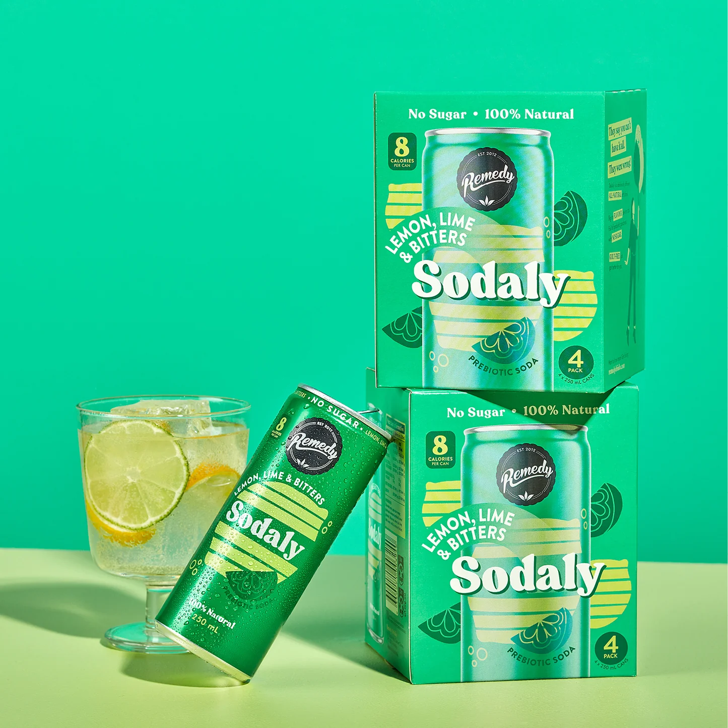 Remedy Sodaly lemon lime bitters cans, boxes with glass of ice, lime; green background.