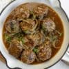 Glazed meatballs with herbs, pineapple, and sesame seeds in a rich sauce served in a bowl.