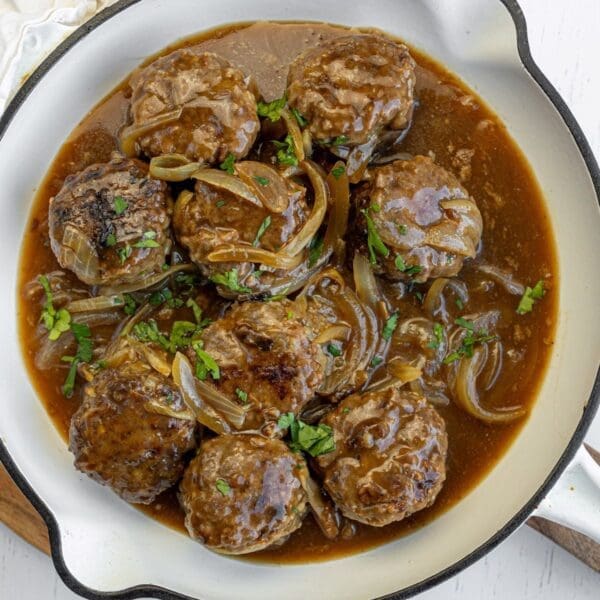 Glazed meatballs with herbs, pineapple, and sesame seeds in a rich sauce served in a bowl.