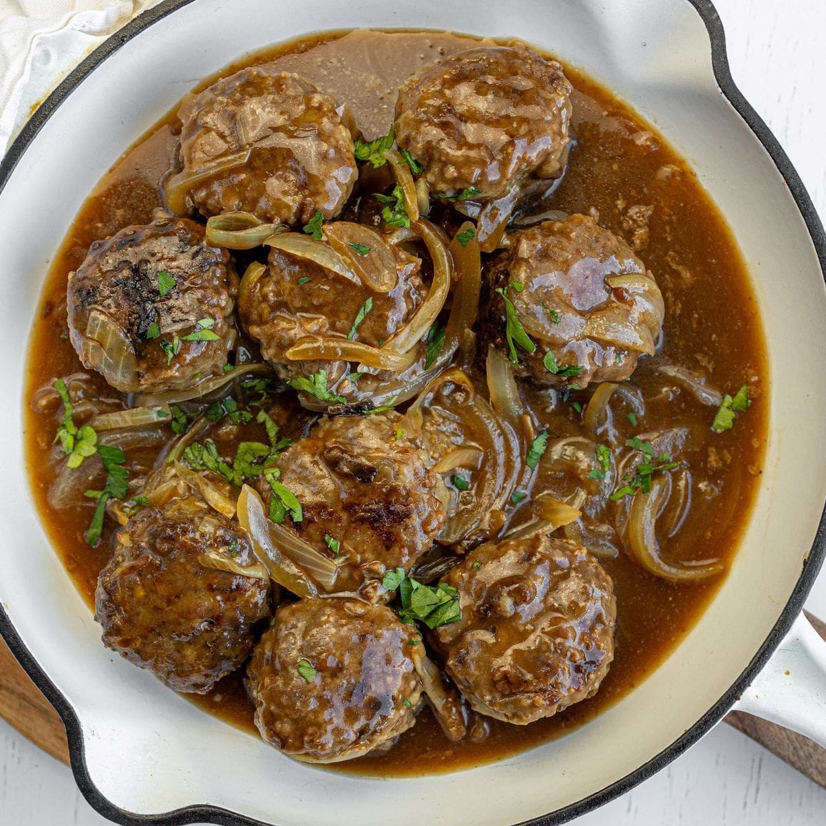 Glazed meatballs with herbs, pineapple, and sesame seeds in a rich sauce served in a bowl.