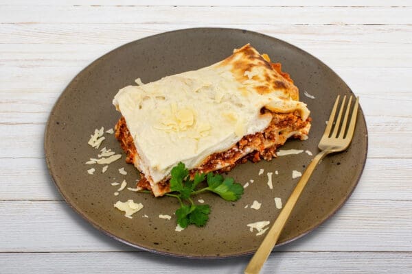 Lasagna slice with cheese flakes on a brown plate, gold fork, and parsley garnish.