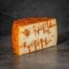 Aged cheese wedge with orange-brown rind, pale interior, and visible lines on a dark surface.