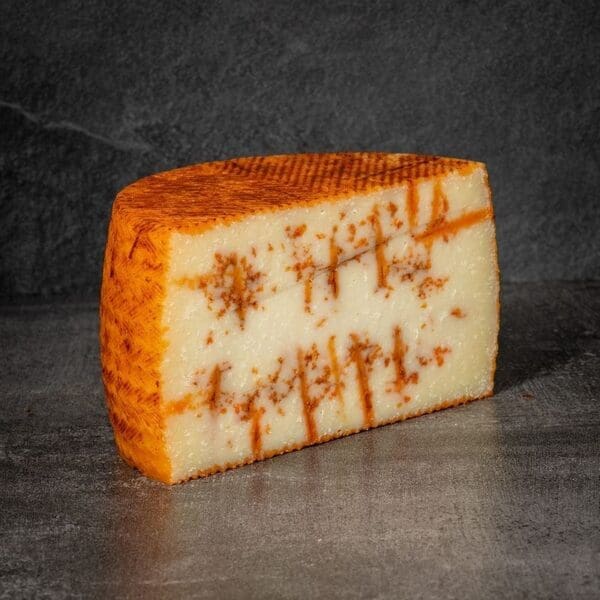 Aged cheese wedge with orange-brown rind, pale interior, and visible lines on a dark surface.