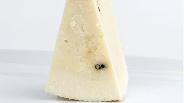 Wedge of hard, aged cheese with crumbly texture and dark spots on off-white surface.