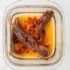 Glass container with anchovy fillets in oil, topped with red chili flakes.