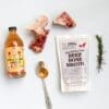 Apple cider vinegar, beef broth pack, beef bones, rosemary, and spoon on white background.