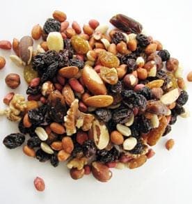 Assorted nuts and dried fruits on a white surface, including almonds, walnuts, and raisins.