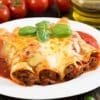 Plate of baked cannelloni with meat, cheese, basil, tomato sauce; tomatoes, olive oil behind.