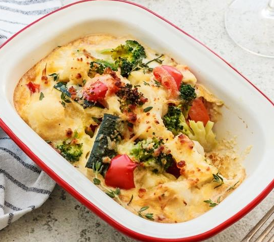 Baked vegetable gratin with broccoli, peppers, zucchini, cheese topping on light surface.