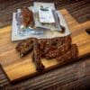 Beef jerky slices with spices on cutting board, vacuum packs in background, rustic setting.