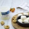 Bowl of bocconcini cheese with bread snacks, tub, tomatoes, and a towel on a wooden board.