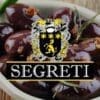 Bowl of dark olives with herbs and spices, featuring a crest and "SEGRETI" in bold letters.