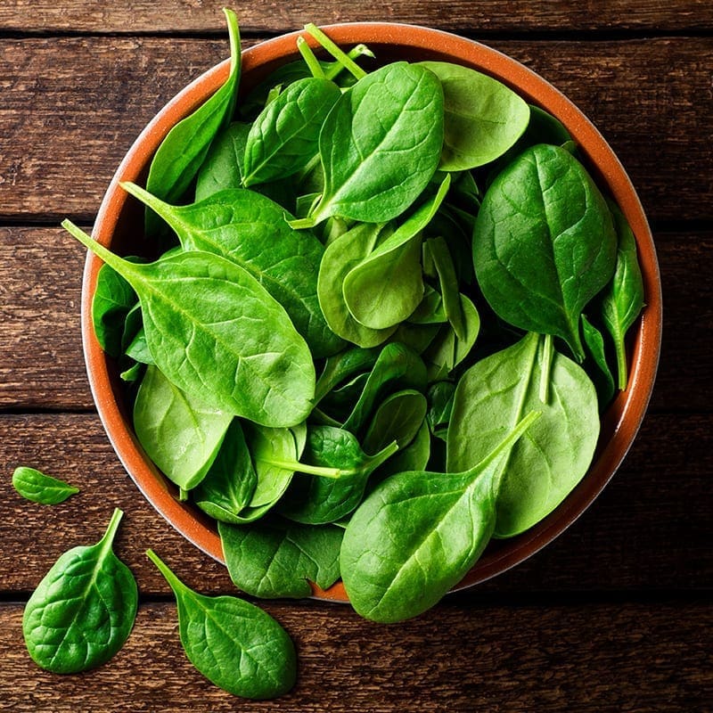 Bowl of fresh spinach leaves on a wooden table.