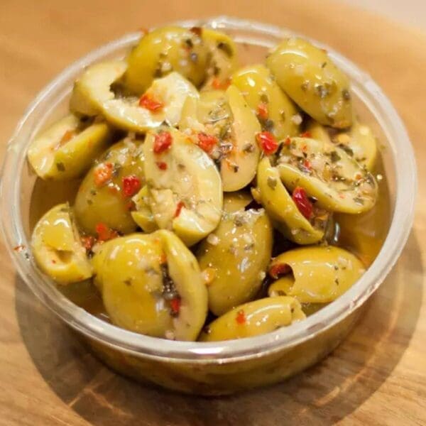 Bowl of sliced green olives with red pepper and herbs in oil dressing.