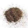 Pile of coarse black pepper granules scattered on white surface.