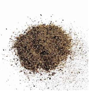 Pile of coarse black pepper granules scattered on white surface.