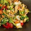 Colorful vegetable stir-fry with bell peppers, broccoli, mushrooms, carrots, onions, and nuts in sauce.