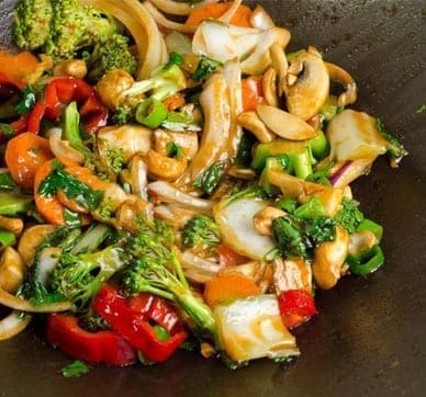 Colorful vegetable stir-fry with bell peppers, broccoli, mushrooms, carrots, onions, and nuts in sauce.