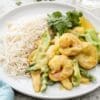 Plate with rice, creamy shrimp curry, assorted vegetables, and cilantro garnish.