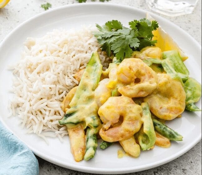 Plate with rice, creamy shrimp curry, assorted vegetables, and cilantro garnish.