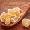 Crystallized ginger pieces on a wooden spoon with a wooden surface background.