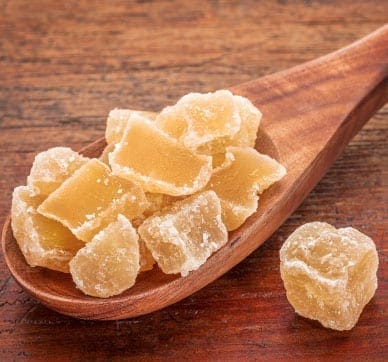 Crystallized ginger pieces on a wooden spoon with a wooden surface background.