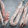 Cured sausages on gray surface, some sliced to show marbled insides and tied with strings.
