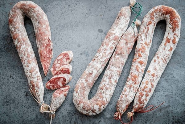 Cured sausages on gray surface, some sliced to show marbled insides and tied with strings.