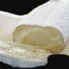 Cylindrical block of soft cheese with white rind, partially cut, on woven surface.