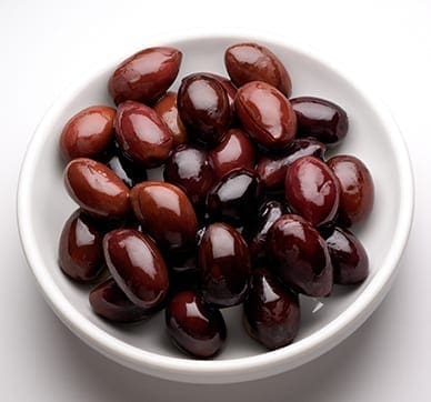 Bowl of dark reddish-brown glossy olives on a white background.