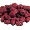 Pile of dried red fruits with wrinkled texture, resembling dates or jujubes, on plain background.