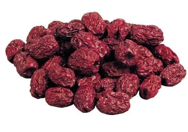 Pile of dried red fruits with wrinkled texture, resembling dates or jujubes, on plain background.