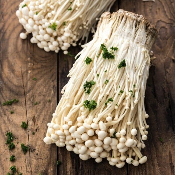 Cluster of enoki mushrooms on wood, garnished with chopped green herbs.