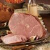 Platter with sliced glazed ham, figs, greens, drinks, and dishes in a festive meal setting.