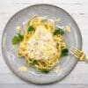 Fettuccine with creamy sauce, diced ham, parsley, shaved cheese, on a gray plate with fork.