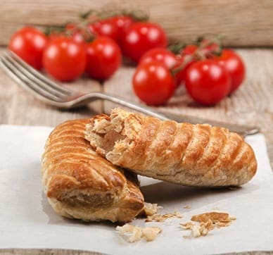 Flaky pastry with sausage filling on parchment, fork and cherry tomatoes in the background.