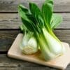 Fresh bok choy with green leaves on a wooden cutting board on a rustic surface.