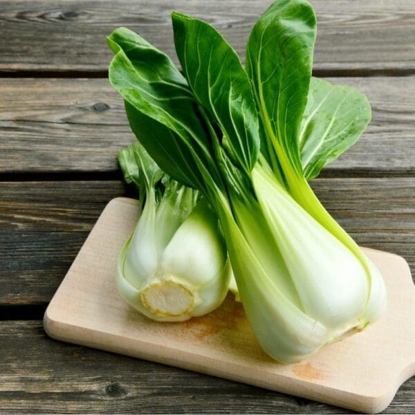 Fresh bok choy with green leaves on a wooden cutting board on a rustic surface.