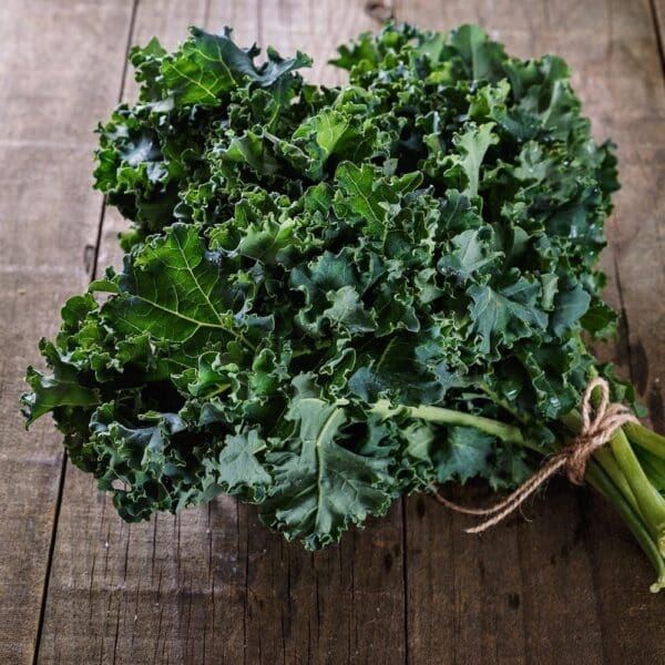 Bunch of fresh, curly kale leaves tied with twine on a wooden surface.