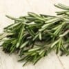 Fresh rosemary sprigs with green, silvery leaves on a light wood surface.