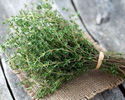 Fresh thyme bundle on burlap, rustic wooden background, small green leaves, thin woody stems.