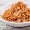 White bowl filled with golden-brown fried onions on wooden surface.