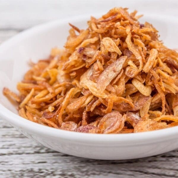 White bowl filled with golden-brown fried onions on wooden surface.