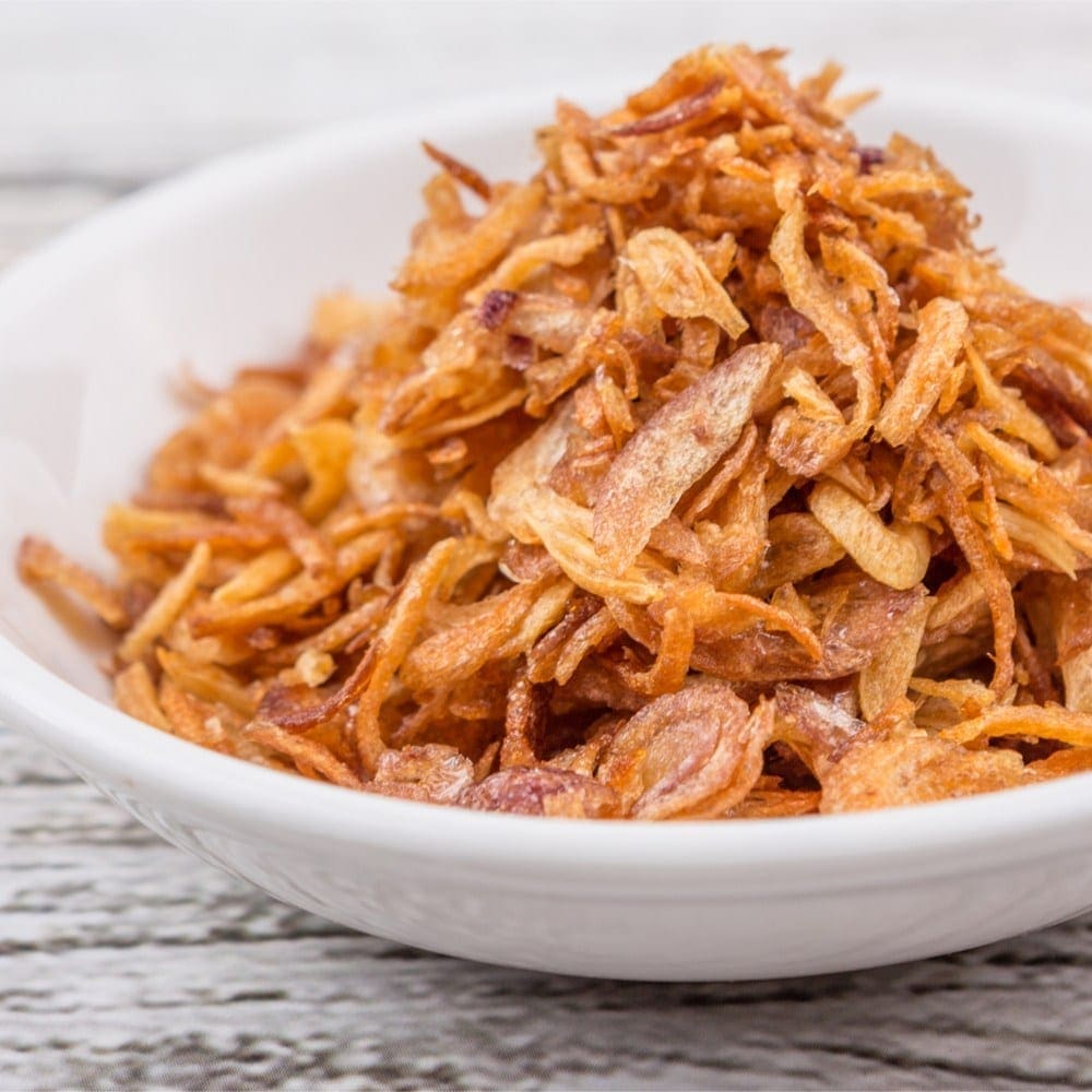 White bowl filled with golden-brown fried onions on wooden surface.