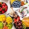 Fruits and cheese platter with strawberries, mangoes, grapes, brie, honey, and nuts on display.