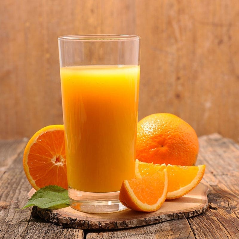 Glass of orange juice with whole and sliced oranges on wooden surface and background.